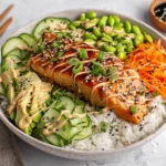 A vibrant teriyaki salmon bowl with rice, avocado, carrots, edamame, and sesame seeds