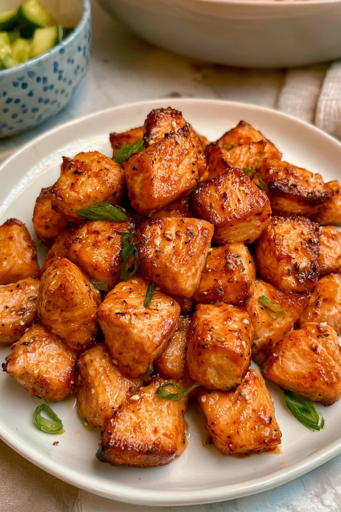 Air fryer salmon bites with browned edges and chopped green onions on a white plate.