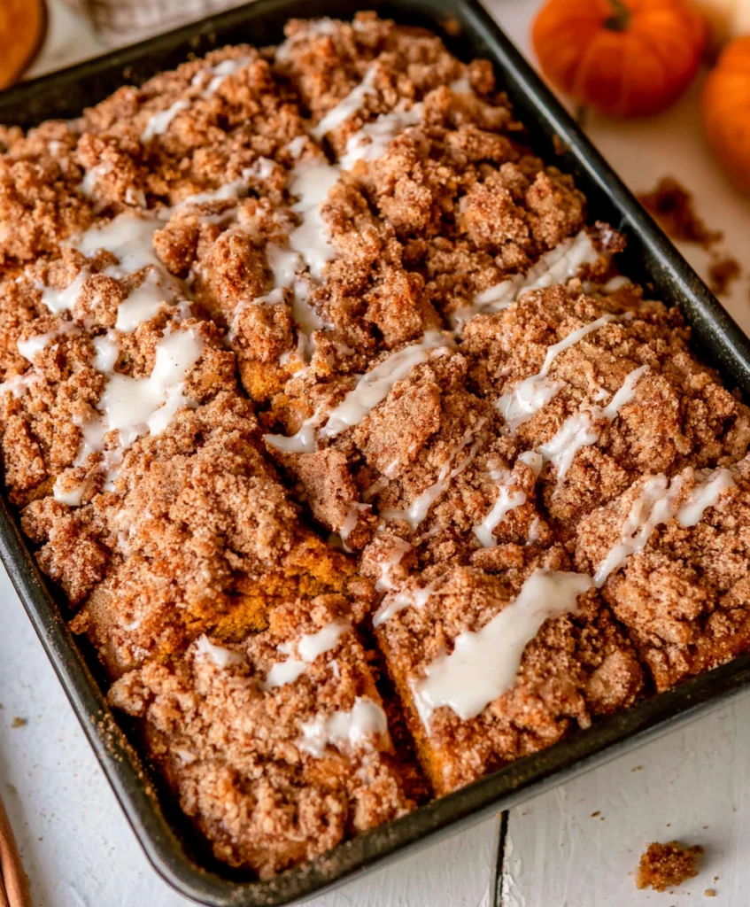 Pumpkin coffee cake with cinnamon streusel and vanilla icing in a black baking pan