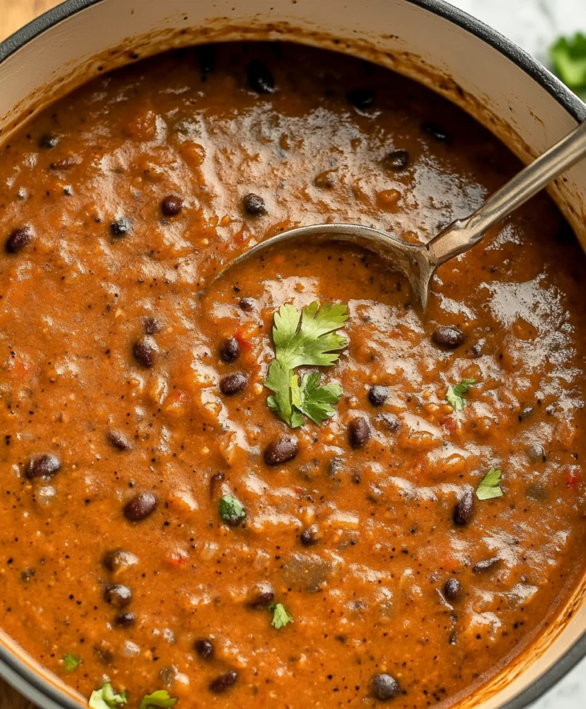 Thick black bean soup with whole beans and cilantro in a pot